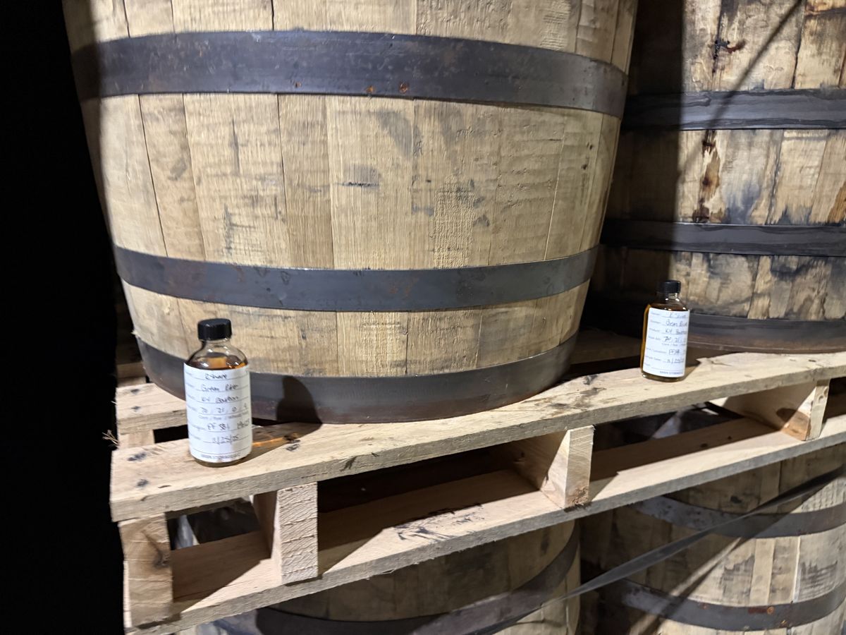 Bourbon sample bottles next to aging barrels